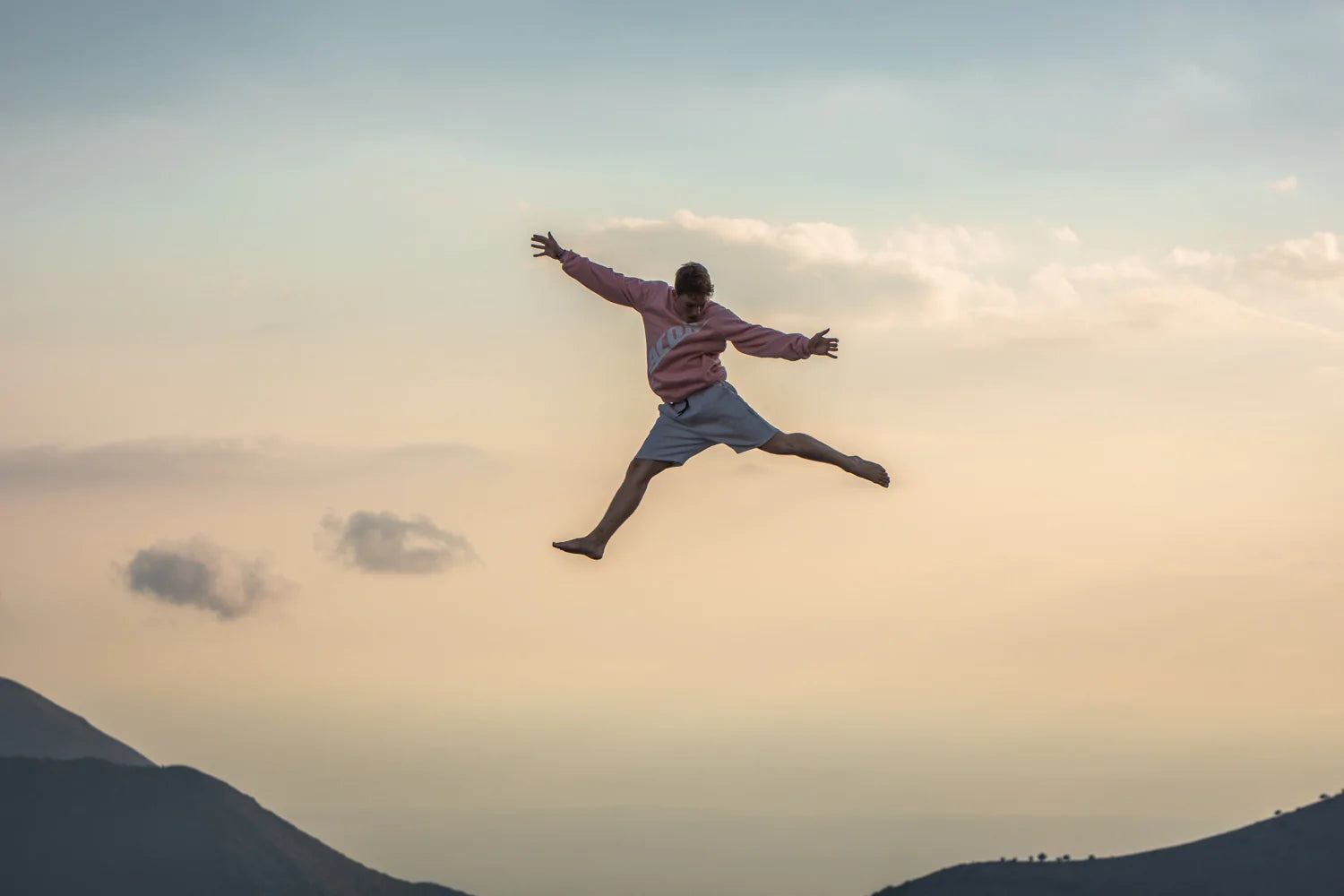 En person som hoppar upp i luften i en rosa Acon-sweatshirt i ett grekiskt landskap