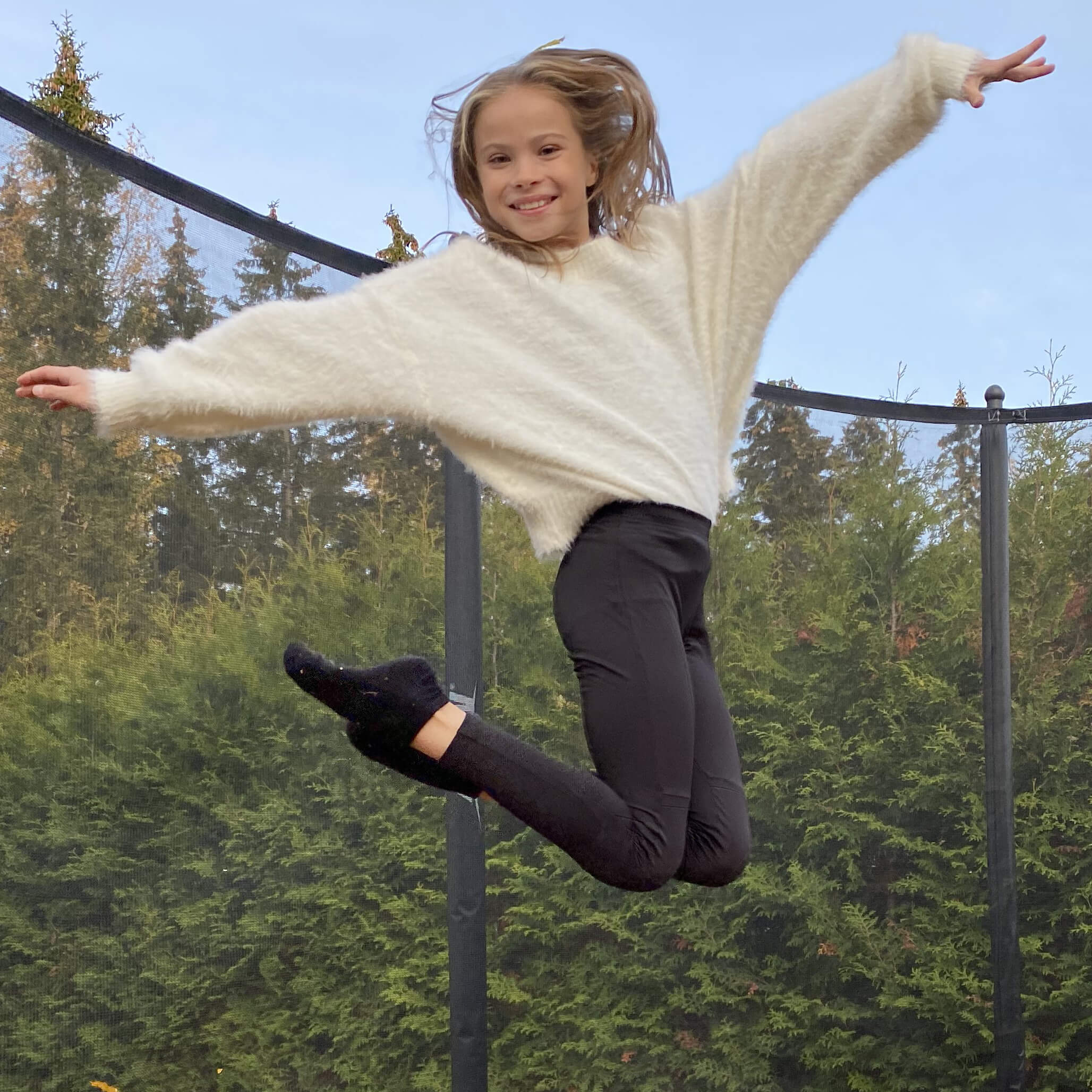 En leende flicka hoppar på en Acon trampolin med skyddsnät