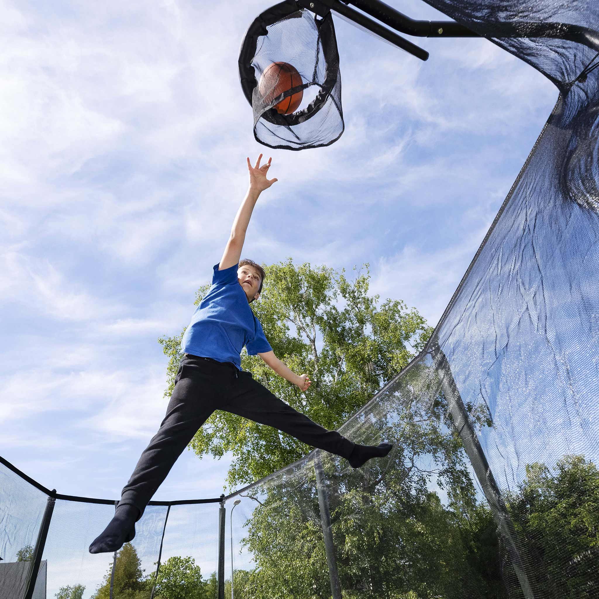 En pojke kastar en basketboll i trampolinens basketkorg.
