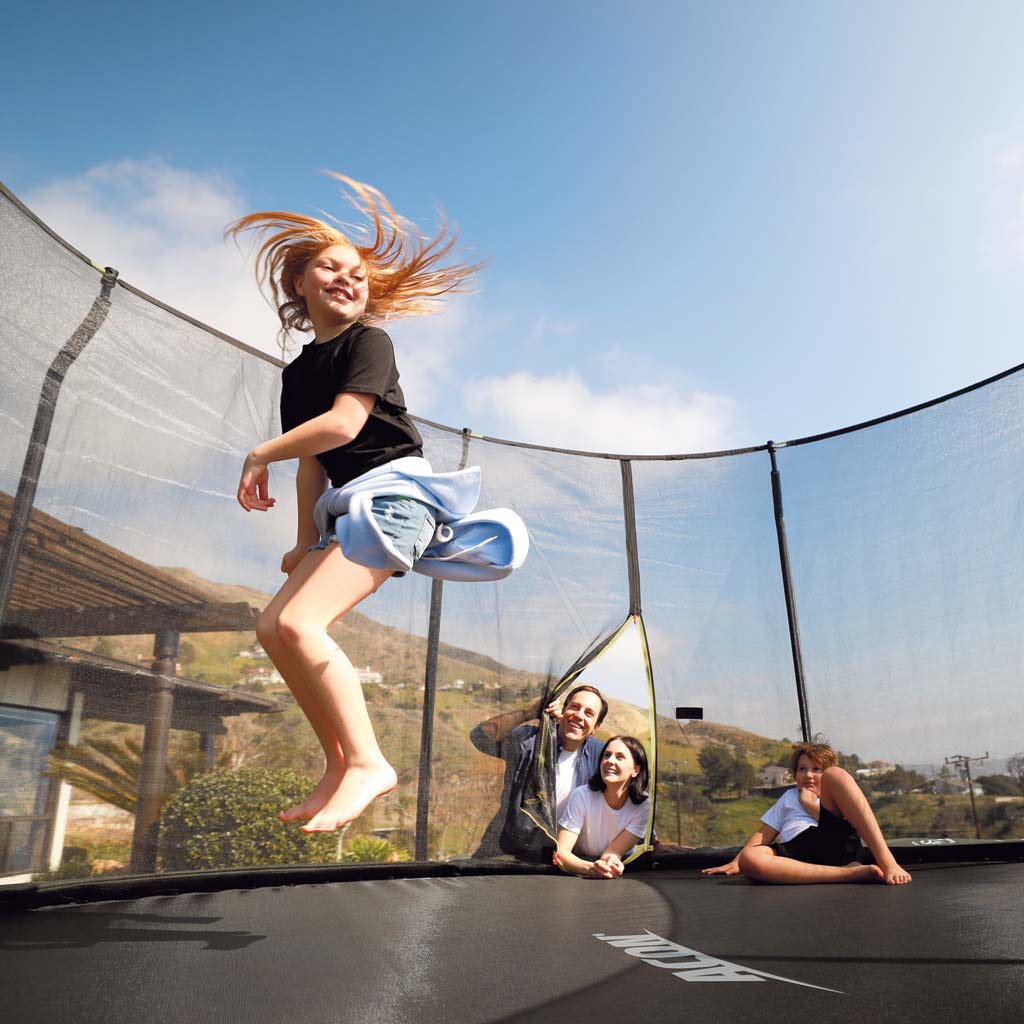 En flicka som hoppar på en Acon-studsmatta och hennes familj som tittar på 