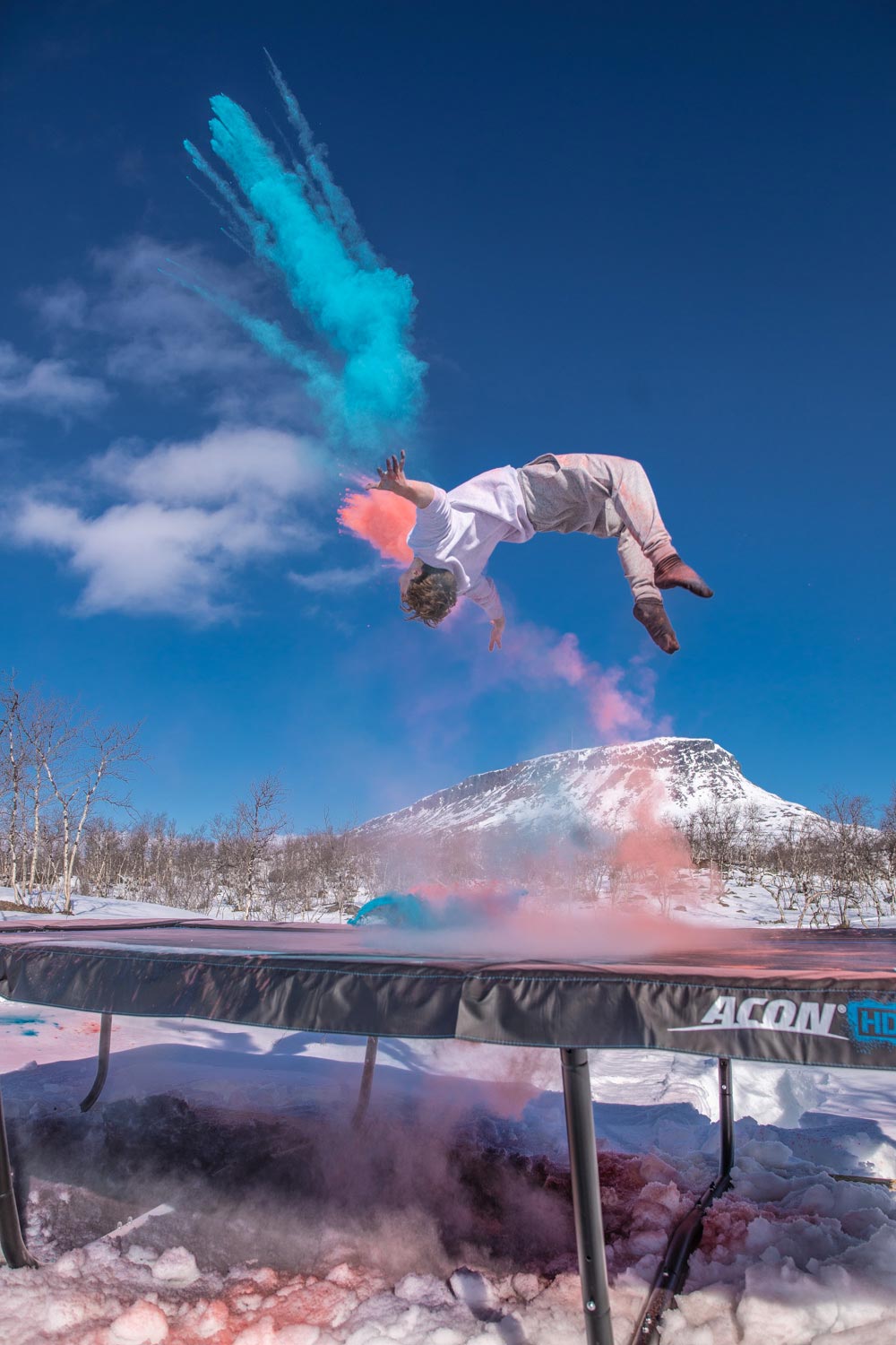 En person som hoppar på en ACON-studsmatta i finska Lappland, med röd och blå rök i bakgrunden 
