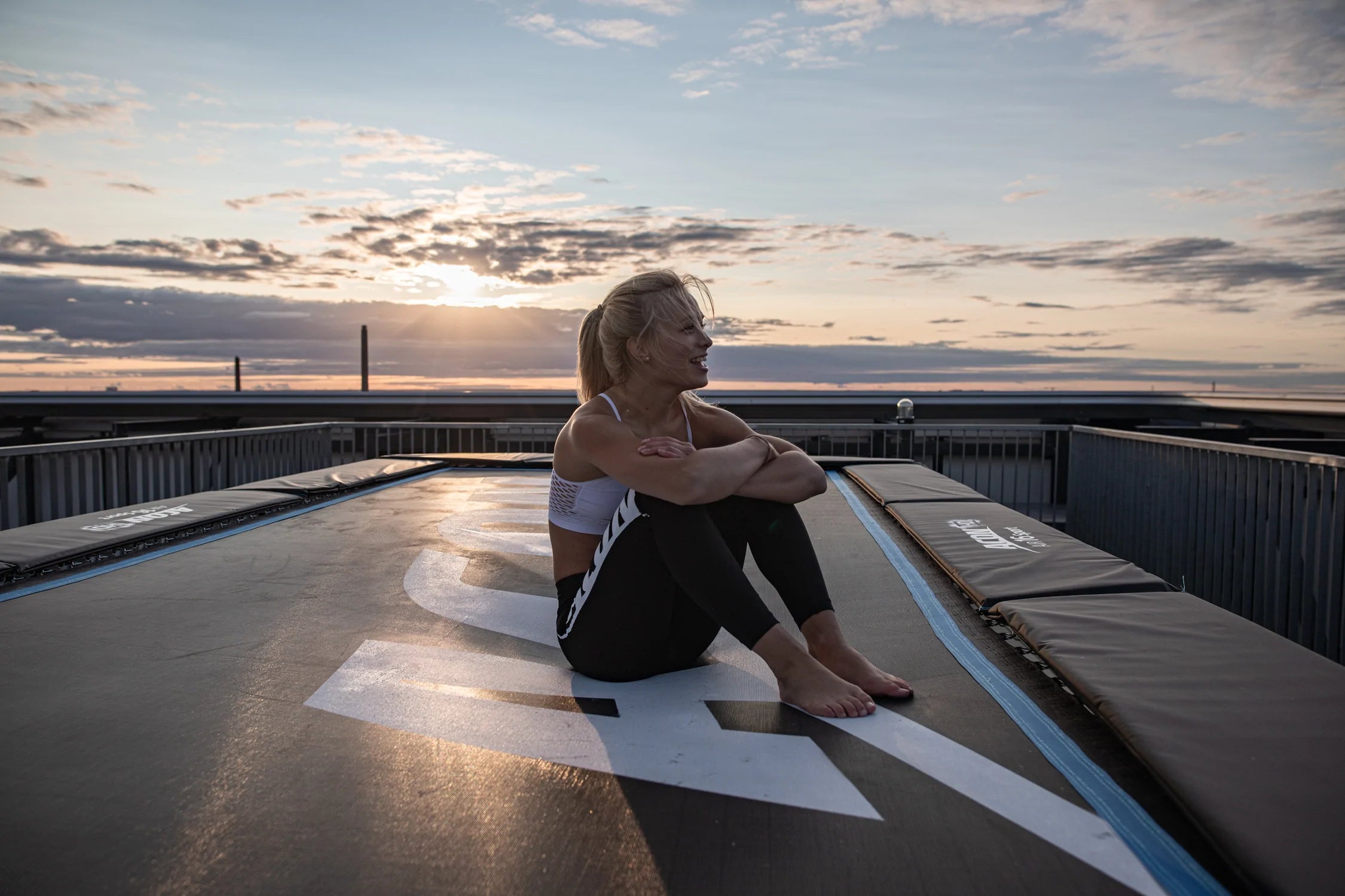 Glad kvinna som sitter på en Acon 16 HD-studsmatta med solnedgång i bakgrunden 