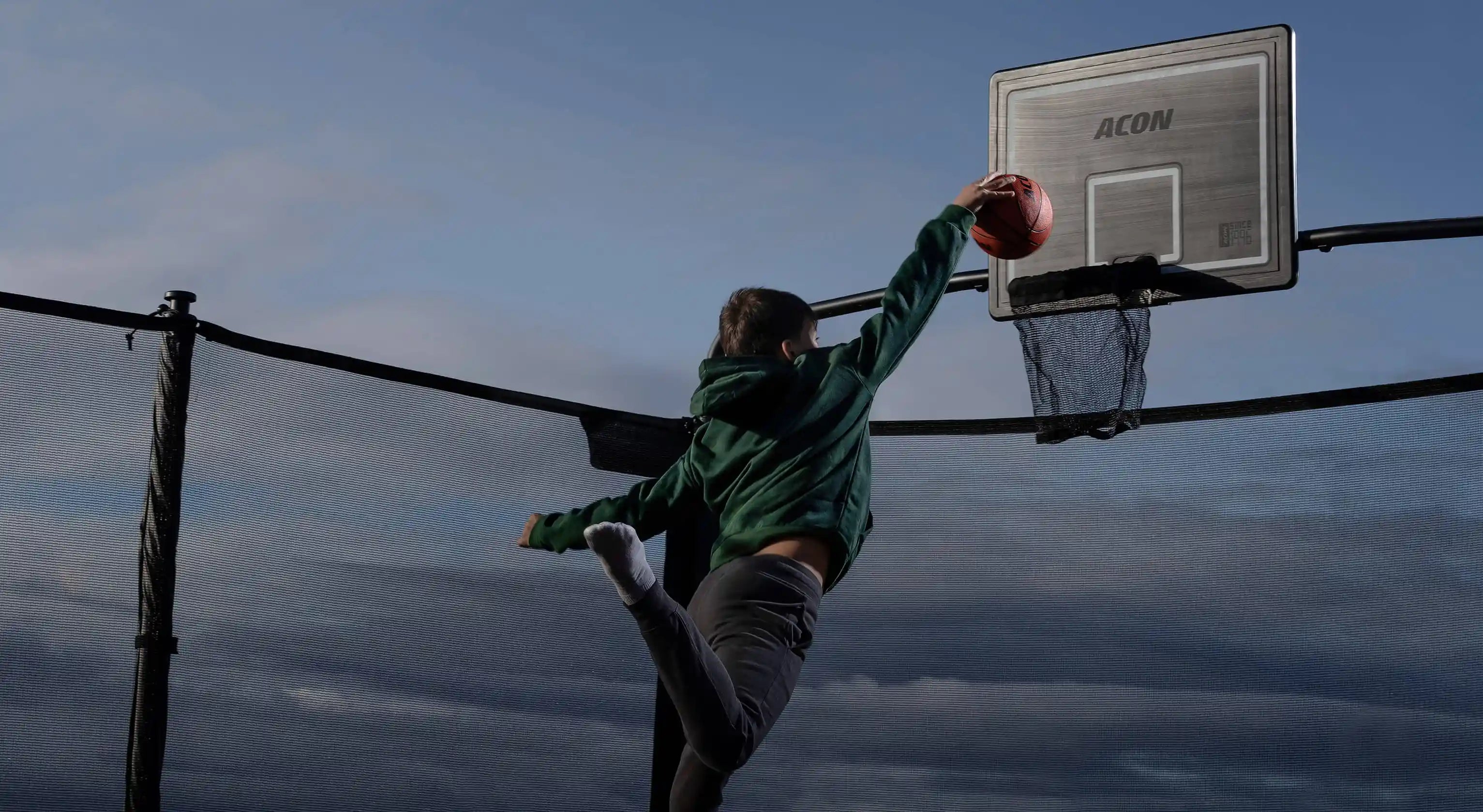 En pojke kastar en basketboll i studsmattans basketkorg.