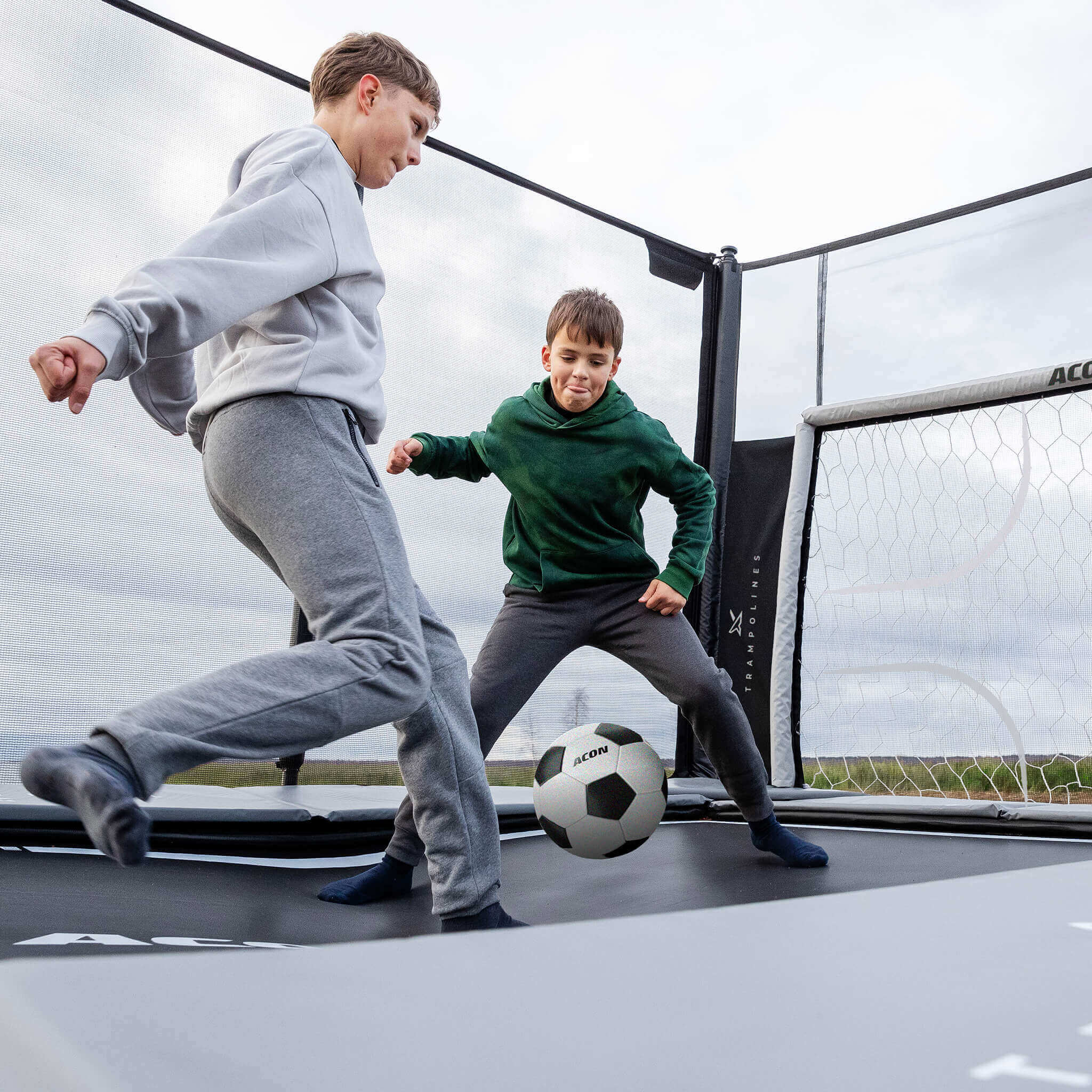 Två pojkar spelar fotboll på en Acon X 17 studsmatta med fotbollsmålning