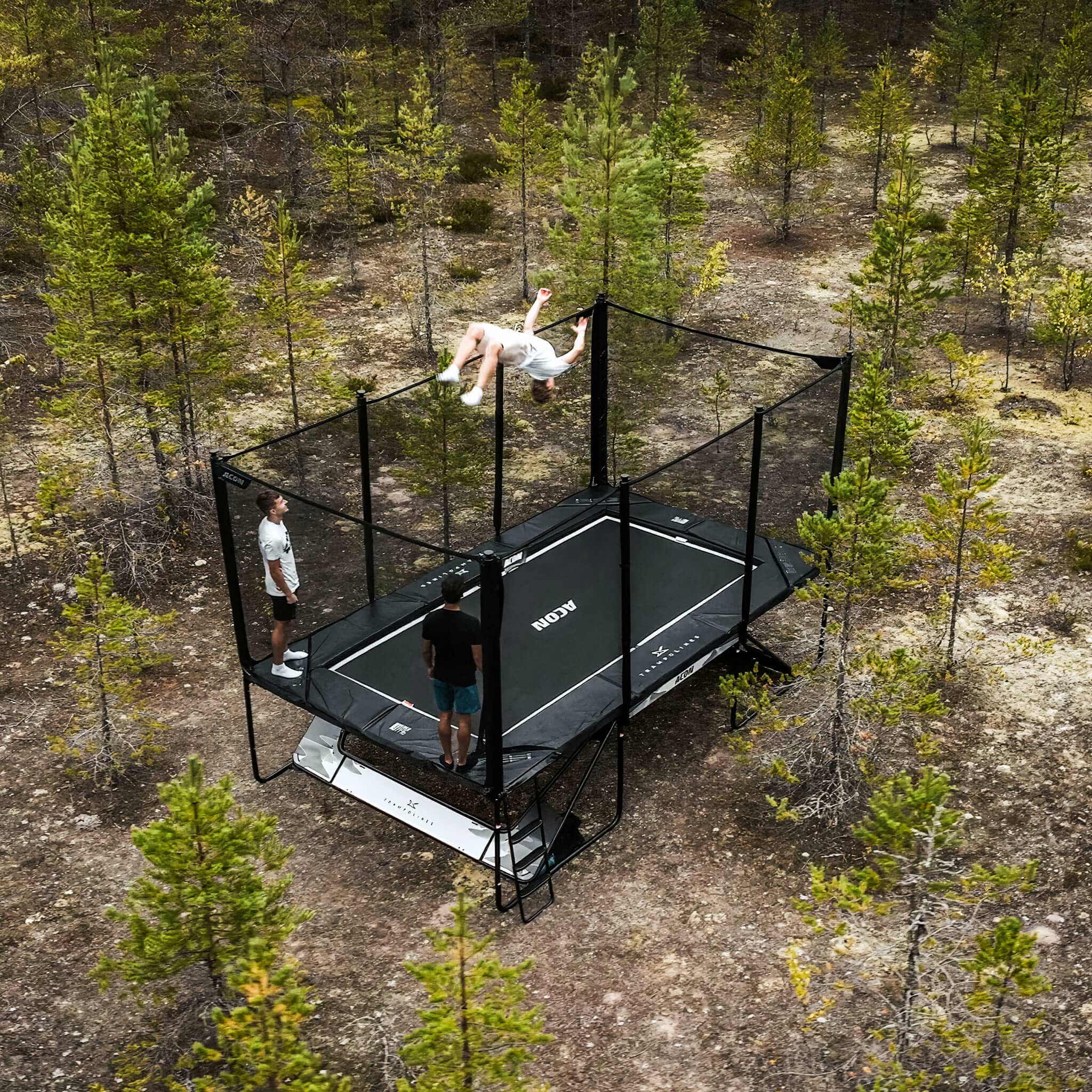 Tre studsmatta trickare på en Acon X-trampolin i en nordisk tallskog.