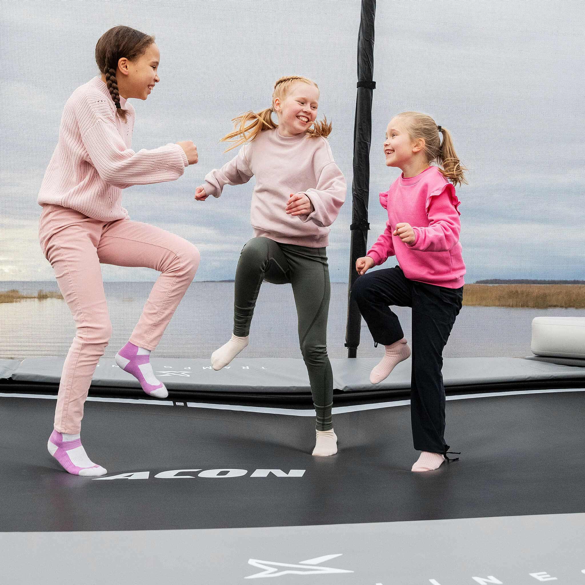 Tre glada flickor i rosa skjortor kliver upp på Acon X studsmattan.