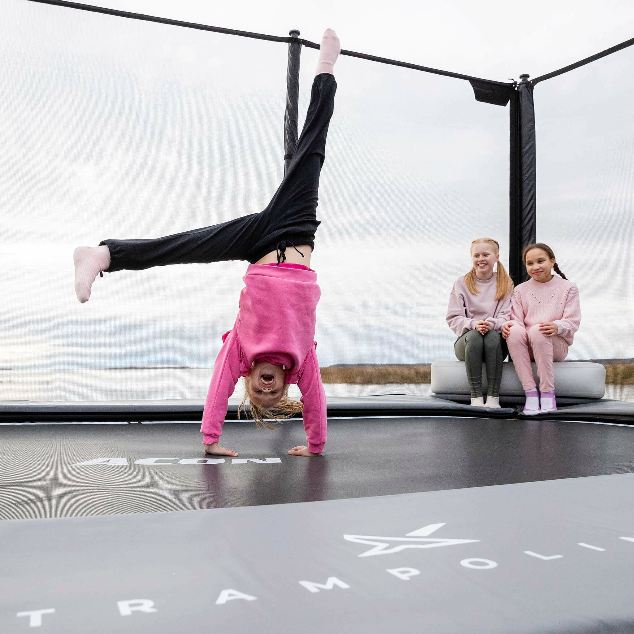 Två flickor sitter på Acon X uppblåsbara triangelblock. Flickan står med händerna på trampolinen.