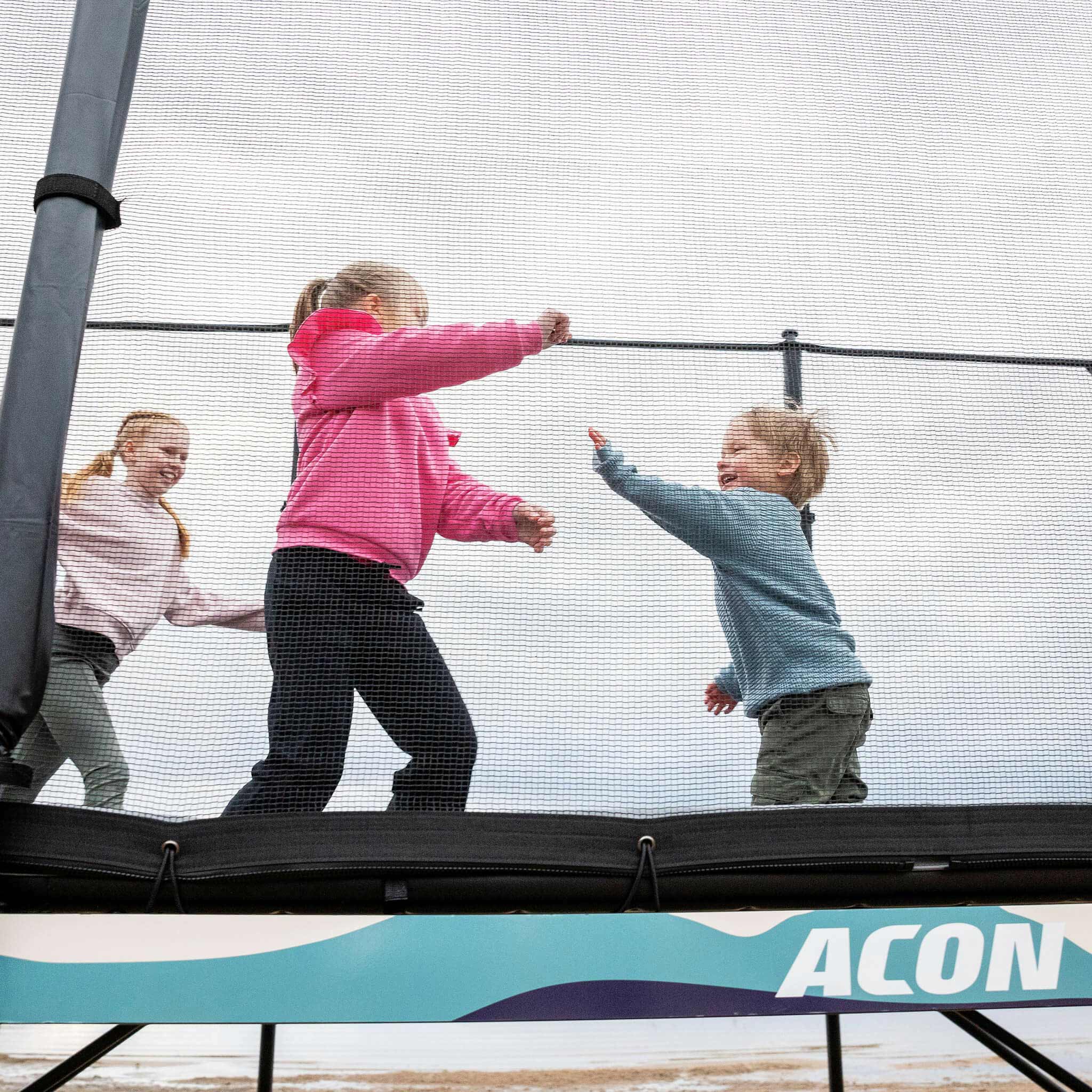 Tre barn leker på Acon X studsmattan.