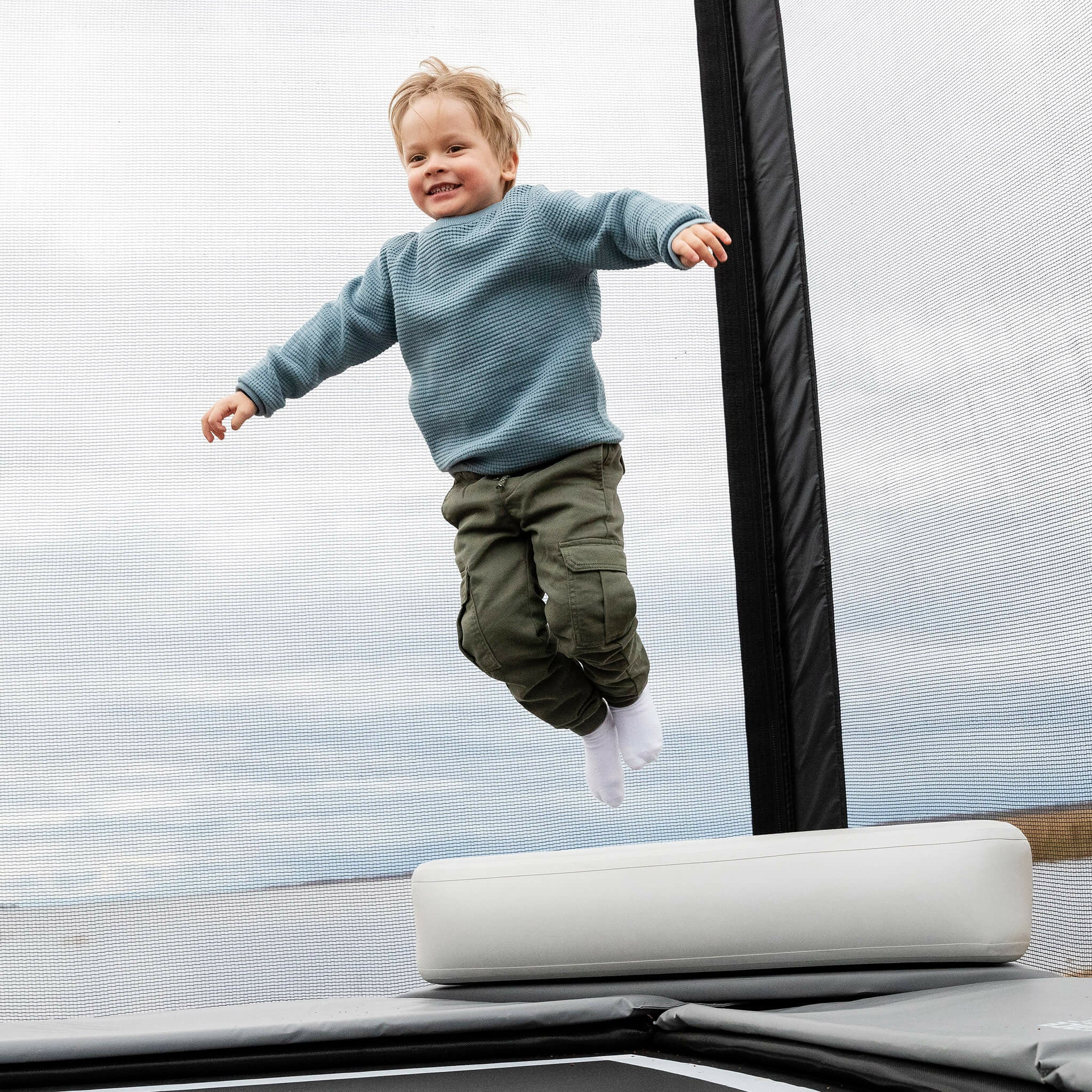 En liten pojke hoppar från toppen av Acon X uppblåsbara triangelblock på en studsmatta.